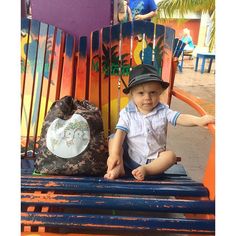 a little boy sitting on top of a wooden bench next to a bag and chair