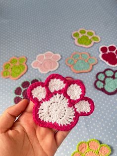 a hand holding a crocheted dog paw in front of many different colored paws