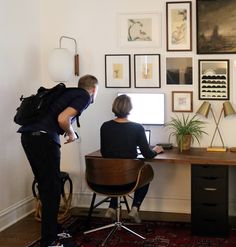 two people are sitting at a desk in front of pictures on the wall and one person is using a laptop