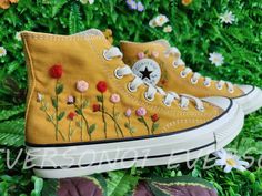 a pair of yellow converse sneakers with flowers on them sitting in the middle of some grass