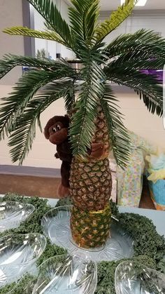 there is a stuffed monkey sitting on top of a pineapple tree in the middle of some plastic plates