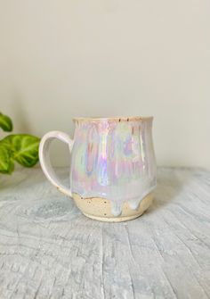 a white and pink coffee cup sitting on top of a table next to a plant