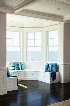 a room with two windows and some blue pillows on the bench in front of it