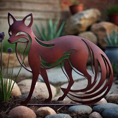 a metal sculpture of a fox standing on top of some rocks next to plants and flowers