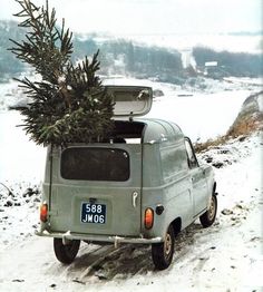 an old car with a christmas tree on the back in the snow by a lake