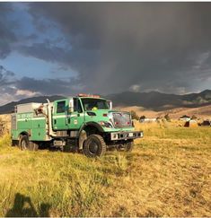 a large green truck parked on top of a dry grass field under a cloudy sky