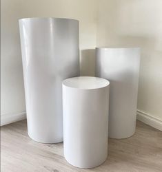 three white vases sitting next to each other on a wooden floor in front of a wall