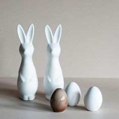 three white ceramic rabbits sitting next to an egg