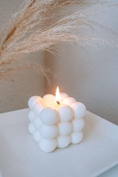 a small white candle sitting on top of a table next to some dry grass and a wall