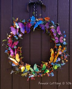 a wreath made out of flowers and butterflies hanging on the front door to welcome guests