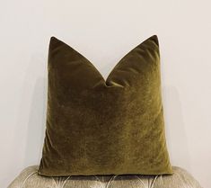 a green velvet pillow sitting on top of a white couch next to a brown chair