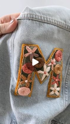 someone is stitching the letter m on their jean pants with flowers and leaves embroidered onto it