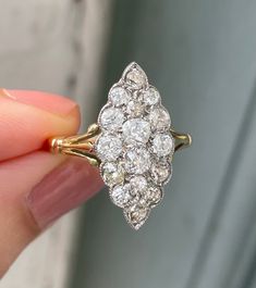 a woman's hand holding an antique diamond cluster ring in yellow gold and white gold