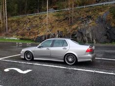 a silver car parked in a parking lot next to a hill with trees on it