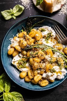 a blue plate topped with pasta covered in cheese and herbs next to a slice of bread