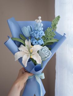 a person holding a bouquet of flowers with blue ribbon around the bottom and white lilies on top