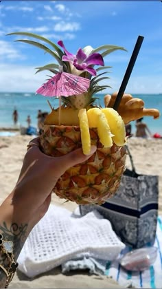 a person holding up a pineapple with some fruit on it at the beach and people in the background