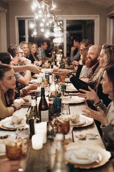 a group of people sitting at a long table with plates and wine glasses on it