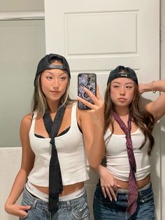 two young women standing next to each other in front of a mirror holding up cell phones