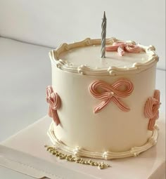 a white cake with pink bows and a single candle