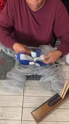 a man sitting at a table making something out of plastic wrappers and wood sticks