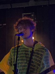 a young man holding a guitar while standing in front of a microphone