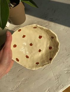 a hand holding a pie pan with strawberries on it, next to a potted plant