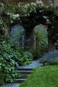 an archway in the middle of a garden with flowers growing on it and steps leading up to it