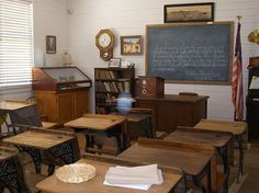 an old school room with desks and books on the wall, clock above them