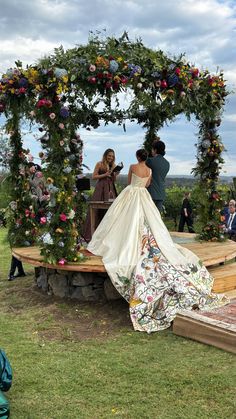 a woman in a wedding dress is standing on a platform with flowers and greenery