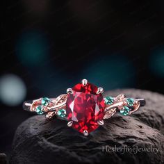 an engagement ring with a red stone surrounded by green and blue stones on top of a rock