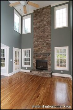 an empty living room with wood floors and stone fireplace in the center, surrounded by windows