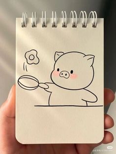 a hand holding a notebook with a drawing of a pig cooking food on the stove