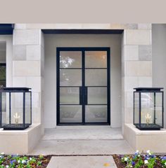 two black lanterns sitting on the side of a white building with flowers in front of it