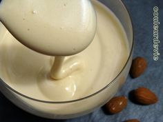 a spoon is pouring almond milk into a glass bowl with almonds on the side