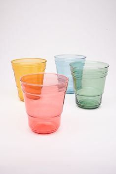 four different colored glass cups sitting next to each other on a white surface, with one empty cup in the middle