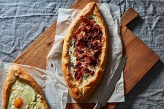 two breads with different toppings sitting on top of a cutting board next to each other