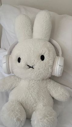 a white stuffed animal with headphones on it's ears sitting on a bed