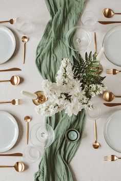 the table is set with white flowers and green napkins, gold cutlery, and silverware