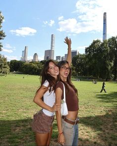 two young women standing next to each other in a park