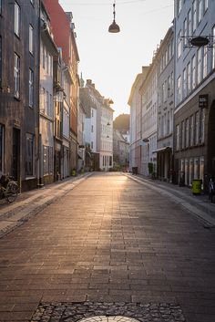 an empty city street with cobblestone pavement and old buildings on both sides at sunset