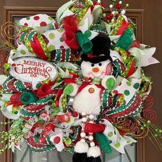 a christmas wreath with a snowman on the front door and green, red and white ribbons