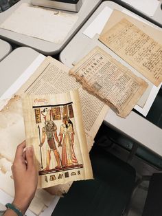 a person is holding an old book in front of some books on a table with other papers