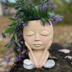 a clay head with purple flowers in it's hair sitting on top of a rock