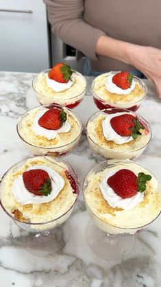 there are many desserts on the table with strawberries in cups next to each other