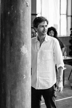 black and white photograph of man standing next to column in large room with people looking on