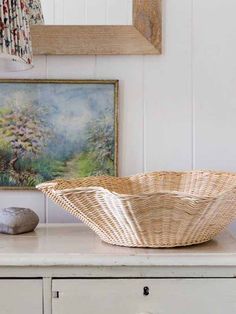 a wicker basket sitting on top of a white dresser next to a painting and lamp