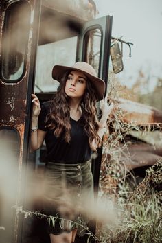 a woman wearing a hat standing in front of an old truck with her hands on the door