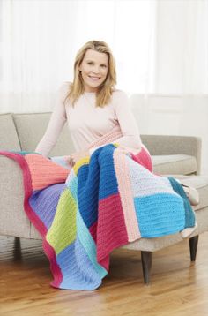 a woman sitting on a couch holding a multicolored blanket