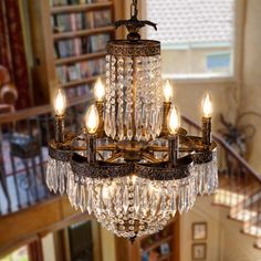 a chandelier hanging from the ceiling in a room with stairs and bookshelves